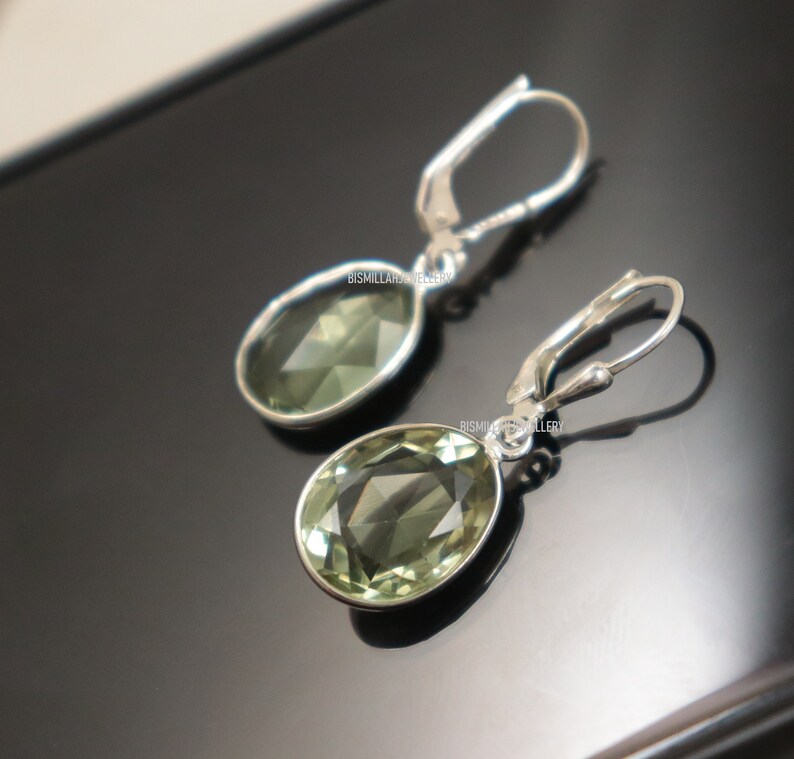 May include: A pair of silver dangle earrings with green oval-shaped gemstones. The earrings have a hook closure.