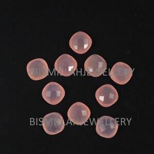 May include: Ten pink gemstone cabochons, each with a faceted surface, arranged in a circular pattern on a black background.
