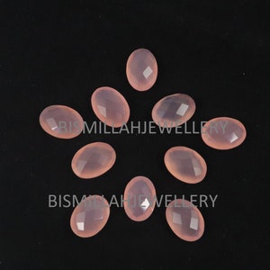 May include: Ten oval-shaped, translucent pink chalcedony gemstones with faceted surfaces. The stones are arranged in a starburst pattern on a black background.