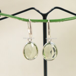 May include: A pair of silver dangle earrings with light green gemstone drops. The earrings are hanging from a black stand.