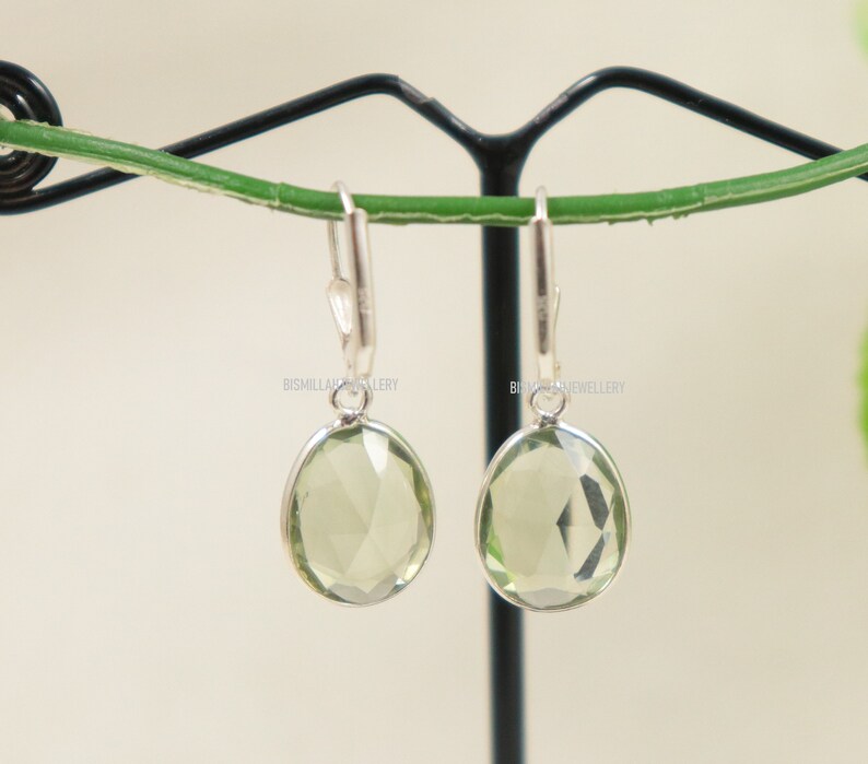May include: A pair of silver dangle earrings with light green gemstone drops. The earrings are hanging from a black stand.