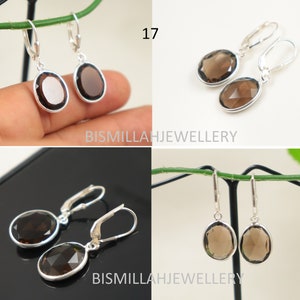 May include: A pair of silver earrings with brown oval-shaped gemstone drops. The earrings have a hook closure. The earrings are displayed on a white background.