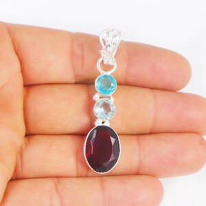 Könnte beinhalten: Silberner Anhänger mit einem roten ovalen Edelstein und drei kleineren blauen Edelsteinen.