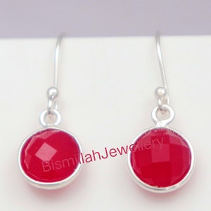 May include: A pair of silver drop earrings with red gemstone drops. The gemstones are faceted and have a shiny finish.