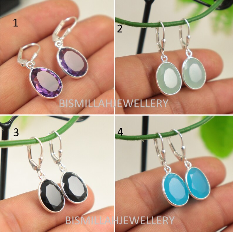 May include: Four pairs of silver dangle earrings with different colored gemstone drops. The earrings are shown on a hand against a green background. The gemstones are amethyst, green, black, and blue.