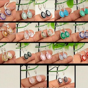 May include: A set of 17 pairs of silver dangle earrings with oval-shaped gemstones. The gemstones are in various colors, including purple, green, blue, red, pink, and clear.