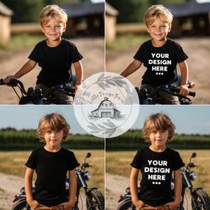 May include: A young boy wearing a black t-shirt with the text "YOUR DESIGN HERE***" printed on it, sitting on a black motorcycle. The boy is smiling and looking at the camera. The motorcycle is parked on a dirt road with green grass and trees in the background.