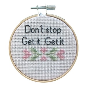 以下が含まれることがあります： 黒い糸で「Don't stop Get it Get it」と書かれたクロスステッチ刺繍枠。ピンクと緑の花柄のアクセントが特徴です。木製の枠は丸く、金属製の締め付け機構が付いています。