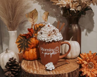 Taza de café de calabaza matutina de color naranja quemado con crema batida artificial y cuchara de madera para decoración otoñal. Bandeja escalonada estilo granja.