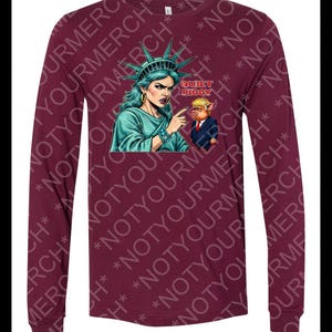 Peut inclure: T-shirt &agrave; manches longues bordeaux avec un dessin de la Statue de la Libert&eacute; pointant vers un cochon en costume, avec le texte "QUIET PIGGY". La Statue de la Libert&eacute; est repr&eacute;sent&eacute;e avec une peau turquoise et une couronne.