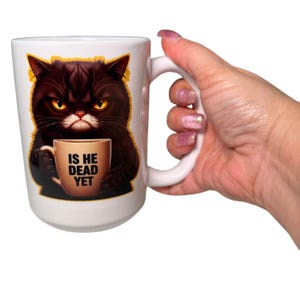 May include: White ceramic mug with a grumpy black cat illustration. The cat holds a coffee cup with the text "IS HE DEAD YET". The cat has yellow eyes and a stern expression. The mug has a large white handle.
