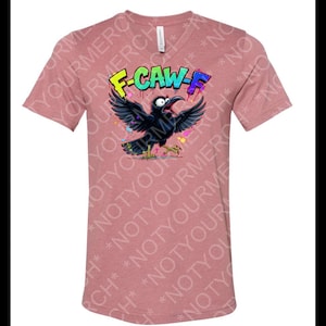 May include: A mauve V-neck t-shirt featuring a cartoon crow with outstretched wings and the text "F-CAW-F" in colorful graffiti style. The crow has a wide open beak and is surrounded by colorful paint splatters.