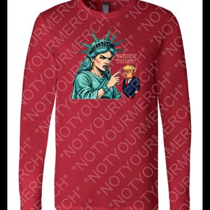 Peut inclure: T-shirt rouge &agrave; manches longues avec un motif de la Statue de la Libert&eacute; pointant vers un cochon en costume. Le texte "QUIET PIGGY" est au-dessus du cochon. Le t-shirt a un col rond et des manches longues.