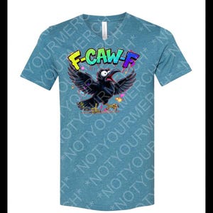 May include: Teal V-neck t-shirt featuring a cartoon crow with outstretched wings and the text "F-CAW-F" in colorful graffiti-style lettering. The crow is black with a red beak and yellow feet. The shirt has a heathered texture.