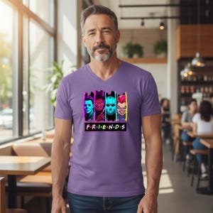 May include: A purple V-neck t-shirt featuring a graphic of four horror movie characters in neon colors. The word "FRIENDS" is printed in white block letters below the characters.