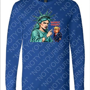 Peut inclure: Un t-shirt bleu &agrave; manches longues avec un dessin de la Statue de la Libert&eacute; pointant vers un cochon en costume avec le texte "Quiet Piggy". La Statue de la Libert&eacute; est repr&eacute;sent&eacute;e avec des cheveux et une robe turquoise.