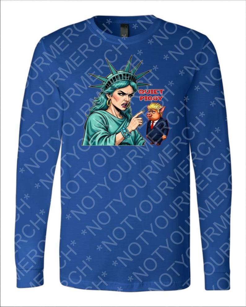 Peut inclure: Un t-shirt bleu &agrave; manches longues avec un dessin de la Statue de la Libert&eacute; pointant vers un cochon en costume avec le texte "Quiet Piggy". La Statue de la Libert&eacute; est repr&eacute;sent&eacute;e avec des cheveux et une robe turquoise.