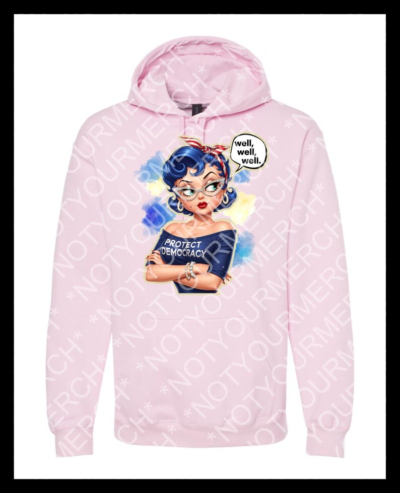 May include: A pale pink hoodie with a graphic of a woman with blue hair, glasses, and a red headband. The graphic includes the text "PROTECT DEMOCRACY" and speech bubbles saying "well, well, well."