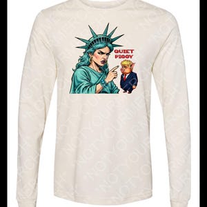 Peut inclure: T-shirt cr&egrave;me &agrave; manches longues avec un dessin de la Statue de la Libert&eacute; pointant vers un cochon en costume. Le texte "QUIET PIGGY" est au-dessus du cochon. La Statue de la Libert&eacute; porte une robe et des bijoux turquoise.