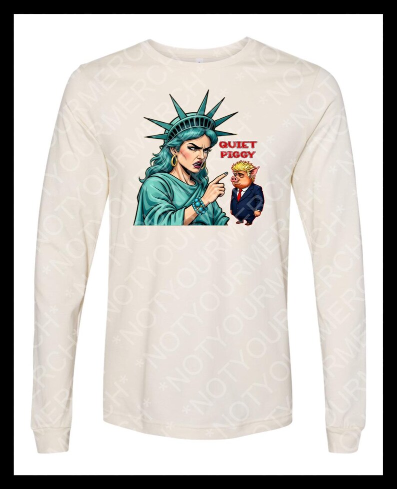 Peut inclure: T-shirt cr&egrave;me &agrave; manches longues avec un dessin de la Statue de la Libert&eacute; pointant vers un cochon en costume. Le texte "QUIET PIGGY" est au-dessus du cochon. La Statue de la Libert&eacute; porte une robe et des bijoux turquoise.