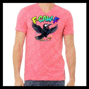 May include: A coral-colored V-neck t-shirt featuring a cartoon crow with outstretched wings and the text "F-CAW-F" in colorful graffiti-style lettering. The crow is black with yellow feet and a wide-open beak.