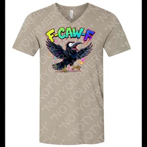 May include: A tan V-neck t-shirt featuring a cartoon crow with open wings and a wide open beak. The crow is black with yellow feet and is surrounded by colorful confetti. The text "F-CAW-F" is above the crow in a graffiti style.