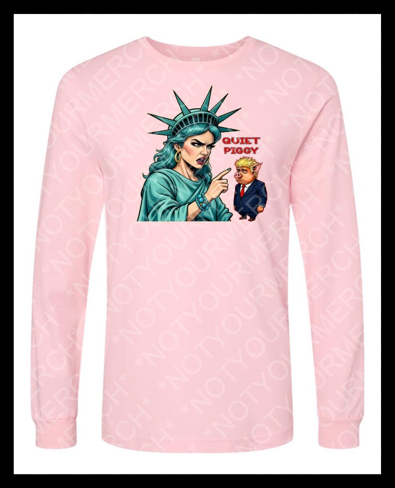 Peut inclure: Un t-shirt rose clair &agrave; manches longues avec un dessin de la Statue de la Libert&eacute; pointant vers un cochon en costume. Le texte "QUIET PIGGY" est au-dessus du cochon. Le t-shirt est &agrave; col rond.
