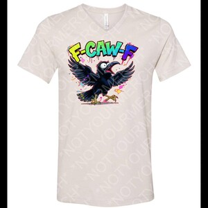 May include: Beige V-neck t-shirt featuring a cartoon crow with open wings and a wide open beak. The crow is black with colorful accents. The text "F-CAW-F" is above the crow in bright colors.