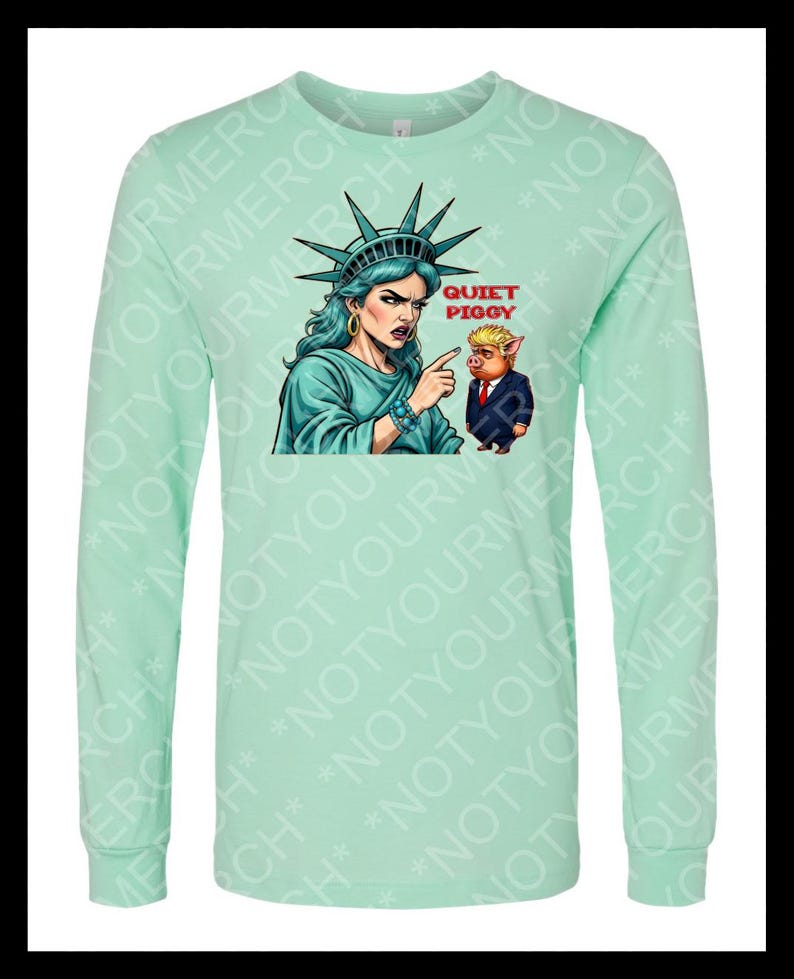 Peut inclure: T-shirt &agrave; manches longues vert menthe avec un dessin de la Statue de la Libert&eacute; pointant vers un cochon en costume. Le texte "QUIET PIGGY" est au-dessus du cochon. Le t-shirt a un col rond et des manches longues.