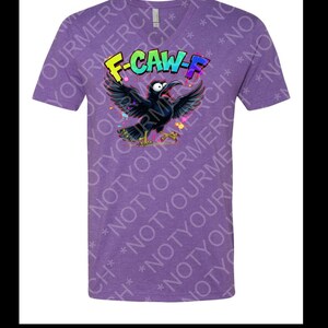 May include: Purple V-neck t-shirt with a cartoon crow graphic. The crow has open wings and a wide open beak. The text "F-CAW-F" is above the crow in colorful letters. The shirt has a heathered texture.