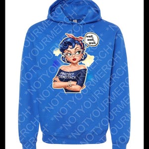 May include: A blue hooded sweatshirt with a graphic of a woman wearing a red headband and glasses. The graphic includes the text "PROTECT DEMOCRACY" and a speech bubble with "well, well, well." The hoodie has a drawstring hood.