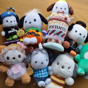 May include: A collection of plush toys featuring a white dog character with different outfits and accessories. The toys include a dog wearing a pumpkin costume, a dog wearing a blue and white plaid shirt, a dog wearing a pink dress, a dog wearing a green costume, and a dog wearing a brown and white striped shirt. The toys are all made of soft, plush fabric and have embroidered details.