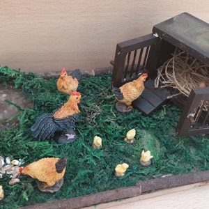 May include: A miniature chicken coop with a brown wooden roof and a wire cage door. There are several small, brown and yellow chickens and chicks surrounding the coop, along with a small pond. The coop is sitting on a bed of green moss.