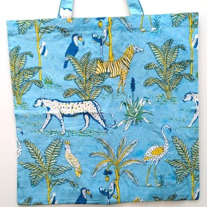 May include: A blue tote bag featuring a jungle scene with zebras, leopards, toucans, and palm trees. The bag has blue handles and a repeating pattern of the jungle animals and foliage. The background is a light blue color.