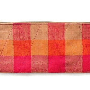 May include: A pink and orange checkered zippered pouch. The pouch is made of a soft, quilted fabric.