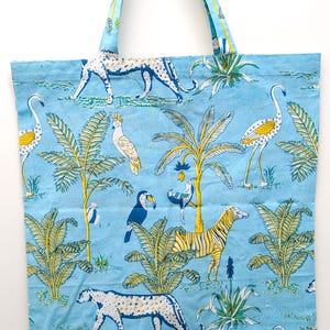May include: Light blue tote bag with a repeating pattern of jungle animals and plants. The design includes leopards, zebras, toucans, and flamingos. The bag has two matching blue handles.