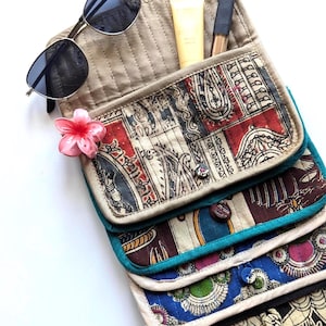 Könnte beinhalten: Ein mehrlagiger Stoff-Organizer mit gesteppten Taschen in verschiedenen Mustern in Rot, Blau, Grün und Schwarz. Er enthält eine Sonnenbrille, eine gelbe Tube, einen schwarzen Kosmetikstift und eine rosa blumenförmige Haarspange.