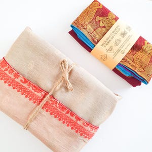 May include: A beige fabric gift wrap with a red and gold border is tied with twine. The wrap is folded and ready to be used. A separate label with the text "Reusable Furoshiki Fabric Gift Wrap" is included.