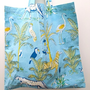 May include: A light blue tote bag with a repeating pattern of zebras, flamingos, toucans, and other tropical animals and plants. The bag has matching blue handles and a simple rectangular shape.