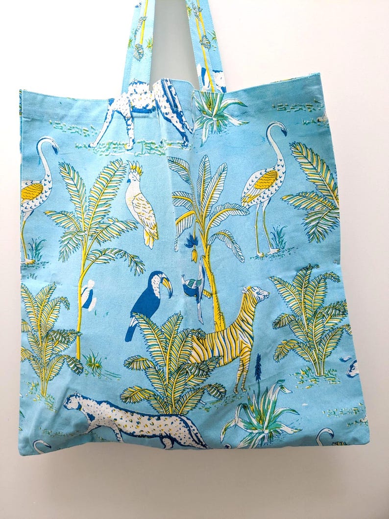 May include: A light blue tote bag with a repeating pattern of zebras, flamingos, toucans, and other tropical animals and plants. The bag has matching blue handles and a simple rectangular shape.