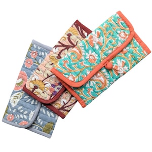 May include: Three quilted fabric cases with floral patterns. One is pale blue with pink flowers, another has a peach and yellow floral design, and the third is teal with orange accents. Each case has a contrasting border.