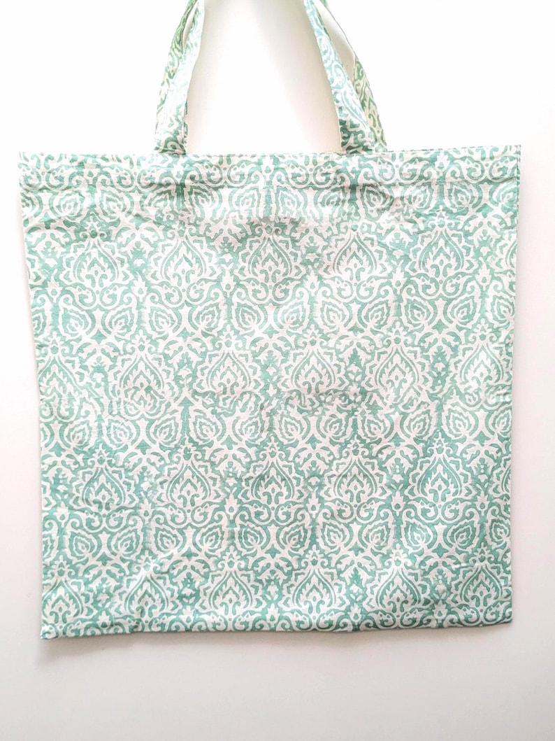 May include: A rectangular tote bag with a repeating white and teal pattern. The bag has two handles made of the same patterned fabric. The pattern is a stylized floral design. The bag is made of a soft fabric.