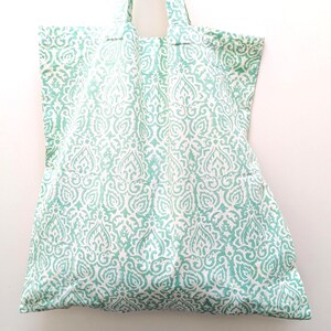 May include: A large tote bag with a repeating white and teal pattern. The bag has two handles and is made of a soft fabric. The pattern is a stylized floral design.
