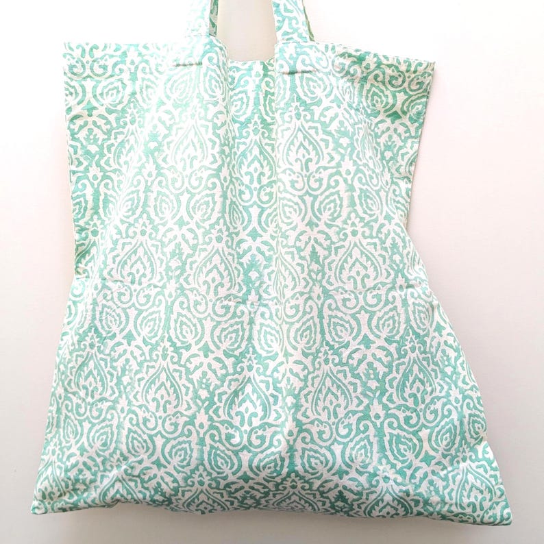 May include: A large tote bag with a repeating white and teal pattern. The bag has two handles and is made of a soft fabric. The pattern is a stylized floral design.