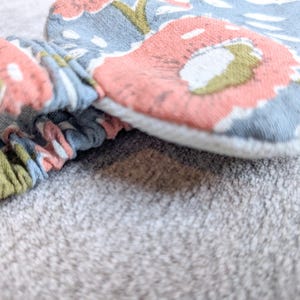 May include: Close-up of a floral patterned headband and matching fabric item. The fabric features a design with pink, blue, and green floral elements. The headband is gathered and elasticized.