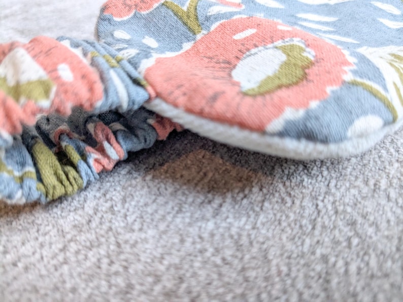 May include: Close-up of a floral patterned headband and matching fabric item. The fabric features a design with pink, blue, and green floral elements. The headband is gathered and elasticized.