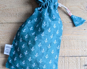May include: A teal drawstring bag with a white leaf pattern. The bag is made of fabric and has a white drawstring closure with a small fabric tassel. The bag is sitting on a wooden surface.