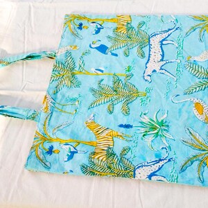 May include: A light blue tote bag with a repeating pattern of yellow palm trees, white and blue animals, and other tropical elements. The bag has a matching blue handle and is made of fabric.