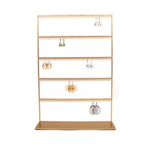 May include: Gold metal earring stand with five tiers for displaying earrings. The stand has a decorative scalloped edge and is empty except for five pairs of earrings.