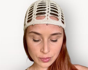 May include: A cream-colored crochet head covering with an open, geometric design. The head covering is adorned with small, silver-colored beads along the front edge. The item is likely handmade and suitable for various occasions.